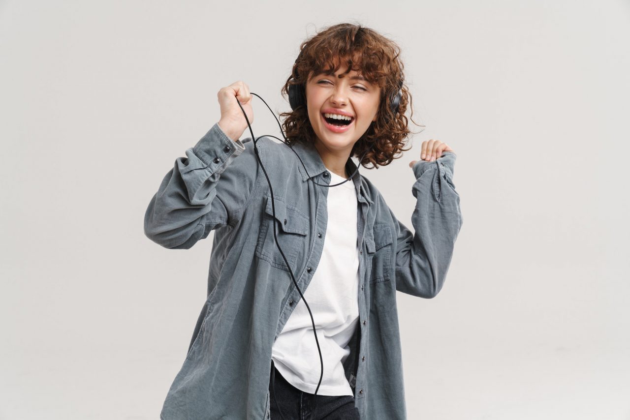 young ginger joyful woman listening music with headphones and dancing.jpg